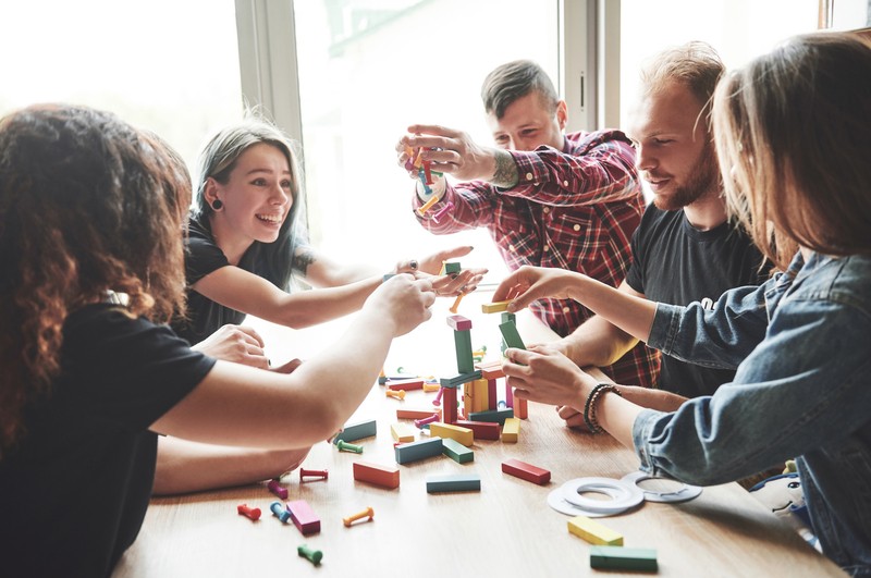 A group of creative friends sitting on a wooden table. People were having fun while playing a board game. | freepik